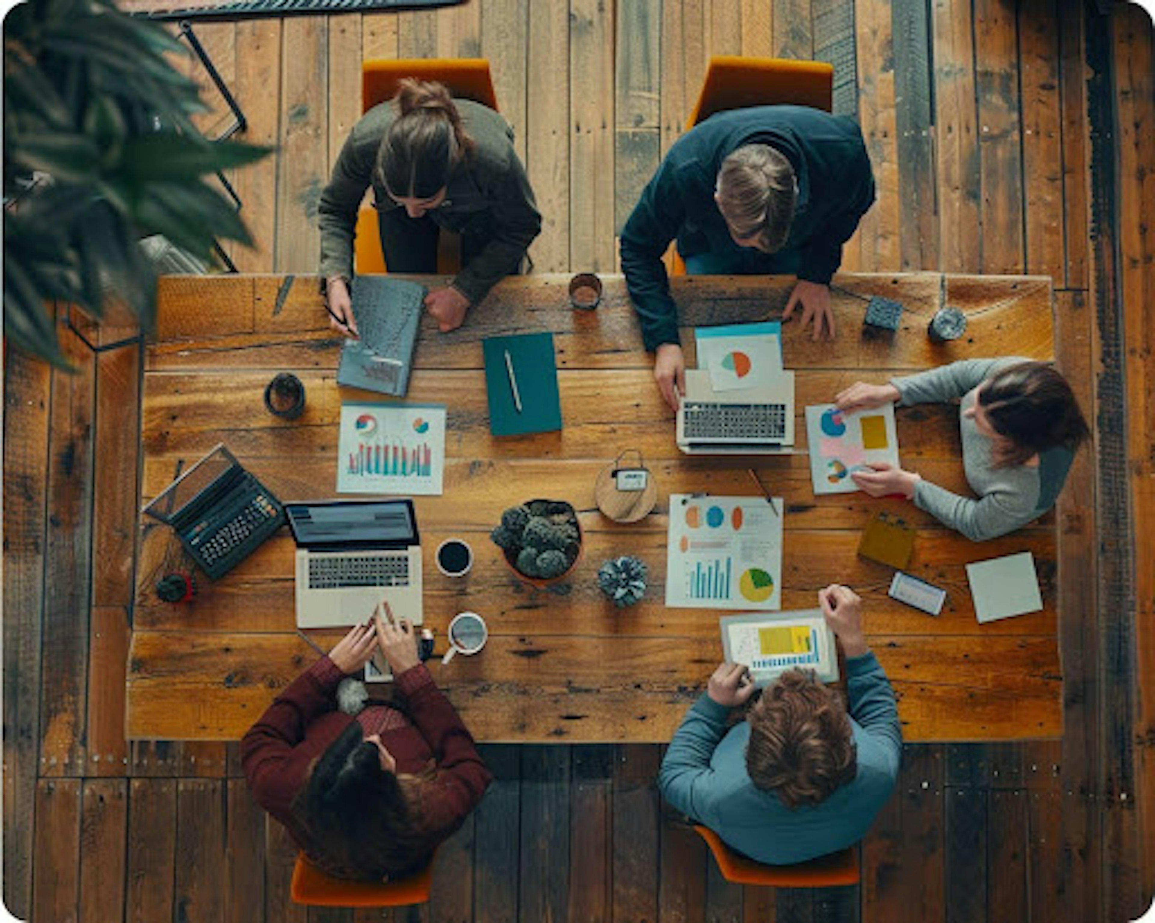 Aerial view of five people sitting at a table with laptops and reports spread around the table.