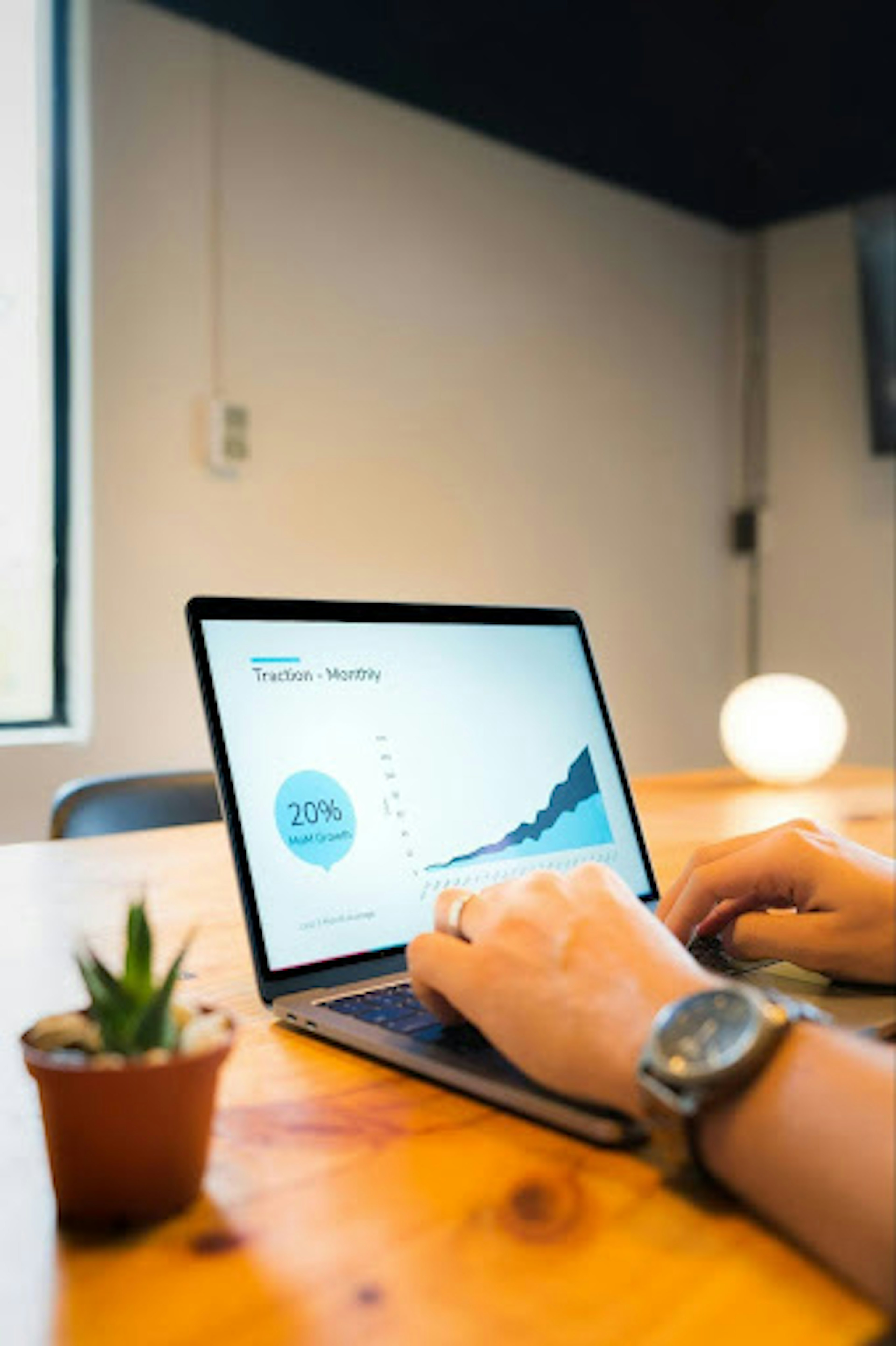 Hands typing on a laptop. The laptop screen contains images of a sales report.