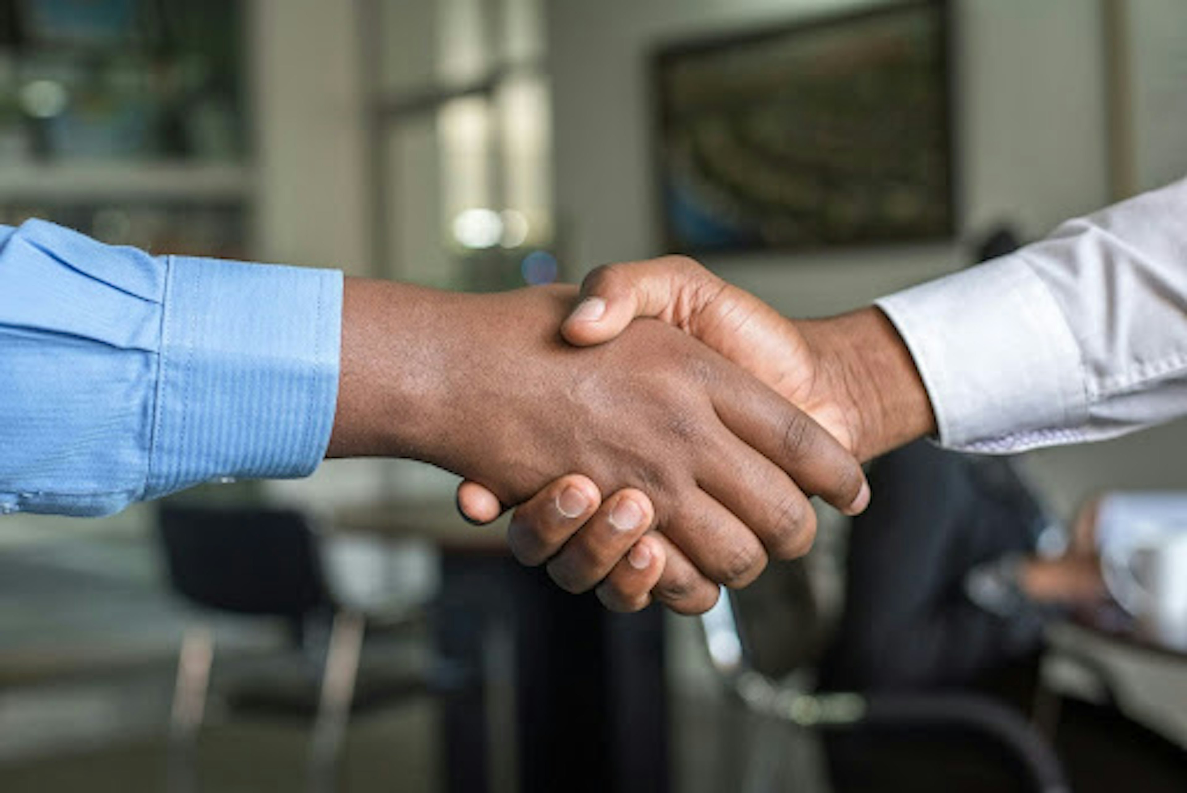 Two arms in dress shirts shaking hands.